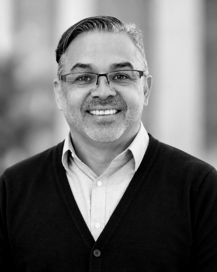 Carlos Jones, smiling, in a dark cardigan and light shirt, photographed outdoors.